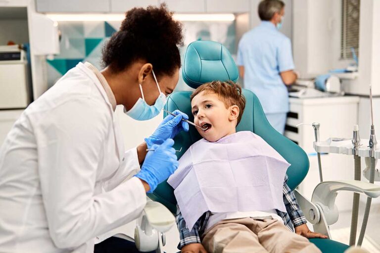 A dental hygienist cleaning an adult patient's teeth in a bright, modern dental office.